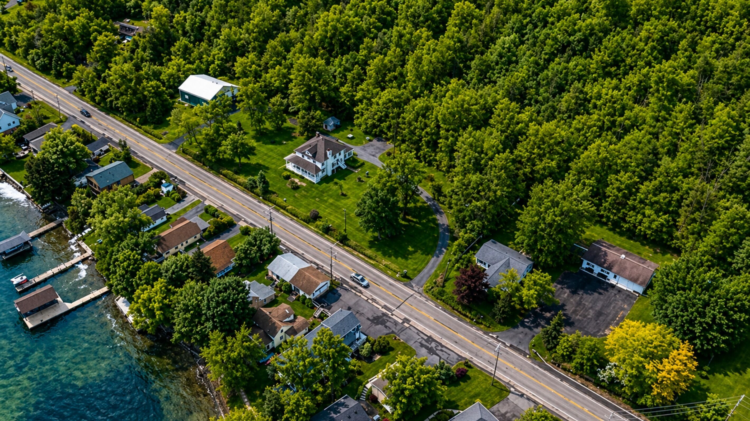 An aerial view of a residential area with houses, a road, and a dock by the water.