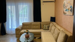 Egy nappali, melyben bézs színű kanapé, egy kerek dohányasztal és egy mennyezeti lámpatest található.