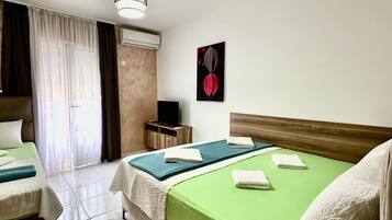 Ein Hotelzimmer mit zwei Betten, einem Fernseher, einer Deckenleuchte und einem Fenster mit Vorhängen.