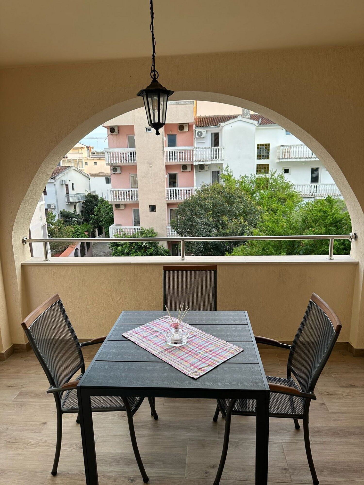 Ein Balkon mit Tisch und Stühlen, einer hängenden Leuchte und Blick auf umliegende Gebäude.