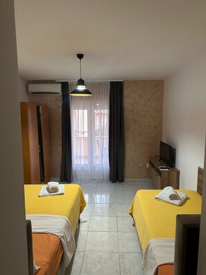 A hotel room with two beds, a television, an air conditioning unit, and a window with curtains. - Il Mare (Budva)