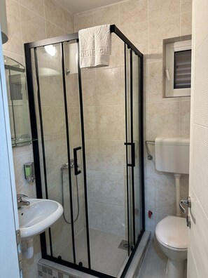 A modern bathroom with a glass-enclosed shower, a white sink, and a toilet. - Il Mare (Budva)