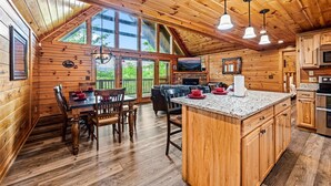 A wooden cabin with a dining area, kitchen, and large windows.