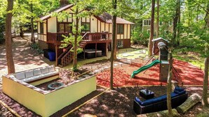 Eine Hütte mit einer Terrasse, einem Whirlpool und einem Spielplatz mit einer Rutsche.