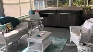 A sunroom with wicker furniture, a hot tub, and large windows. - Lakeview Designer Home in Valle Verde Village (Lady Lake)