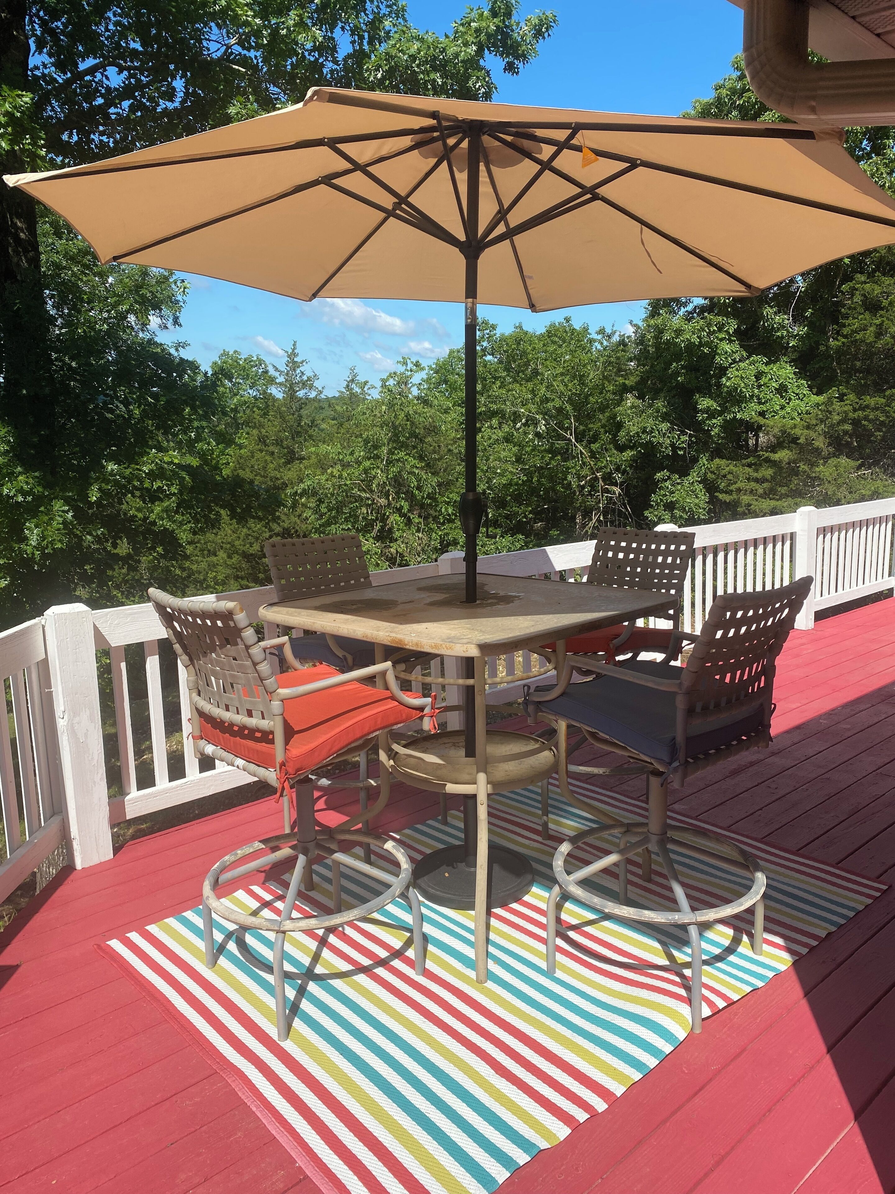 Eine Terrasse mit Tisch und Stühlen, einem Streifenmuster-Teppich und einem großen Sonnenschirm.