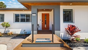 A modern house with a number 209 sign, a wooden deck, and a small garden with various plants. - Fancy That: Pool, Putting Green, 1.5 Blocks to Beach by Anna Maria Life Vacation Rentals (Holmes Beach)