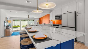 A modern kitchen with a large island, white cabinets, and a blue accent wall. - Fancy That: Pool, Putting Green, 1.5 Blocks to Beach by Anna Maria Life Vacation Rentals (Holmes Beach)