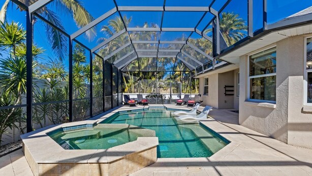 A swimming pool with a glass enclosure, surrounded by lounge chairs and palm trees.
