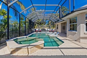 Une piscine entourée d’une structure en verre, avec des chaises longues et des palmiers tout autour.