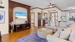 A spacious living room with a large flat-screen TV, a wooden entertainment unit, a round coffee table, and a comfortable sofa set.