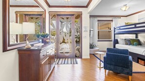 A hotel room with a wooden dresser, a desk with a lamp, a bunk bed, and a large mirror.