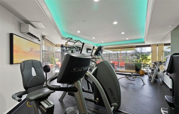 Une salle de sport équipée d’appareils de cardio, d’un climatiseur fixé au mur et d’une grande fenêtre donnant sur l’extérieur.