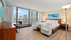 A hotel room with a large bed, two armchairs, a wooden desk, and a view of the city through large windows.