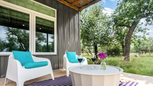 Een moderne buitenzitplaats met witte stoelen en een ronde tafel, met uitzicht op een weelderige tuin en bomen.