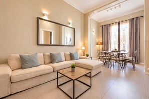 A modern living room with a sofa, a coffee table, a dining area with chairs, and a large mirror on the wall.