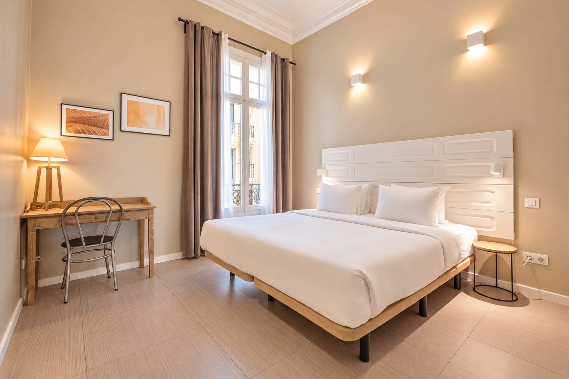 A hotel room with a bed, a desk, a chair, and a window with curtains.