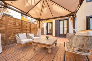 An outdoor patio with wicker furniture, a wooden table, and a large umbrella providing shade. - Sweett | Sepulveda Principal C (Barcelona)