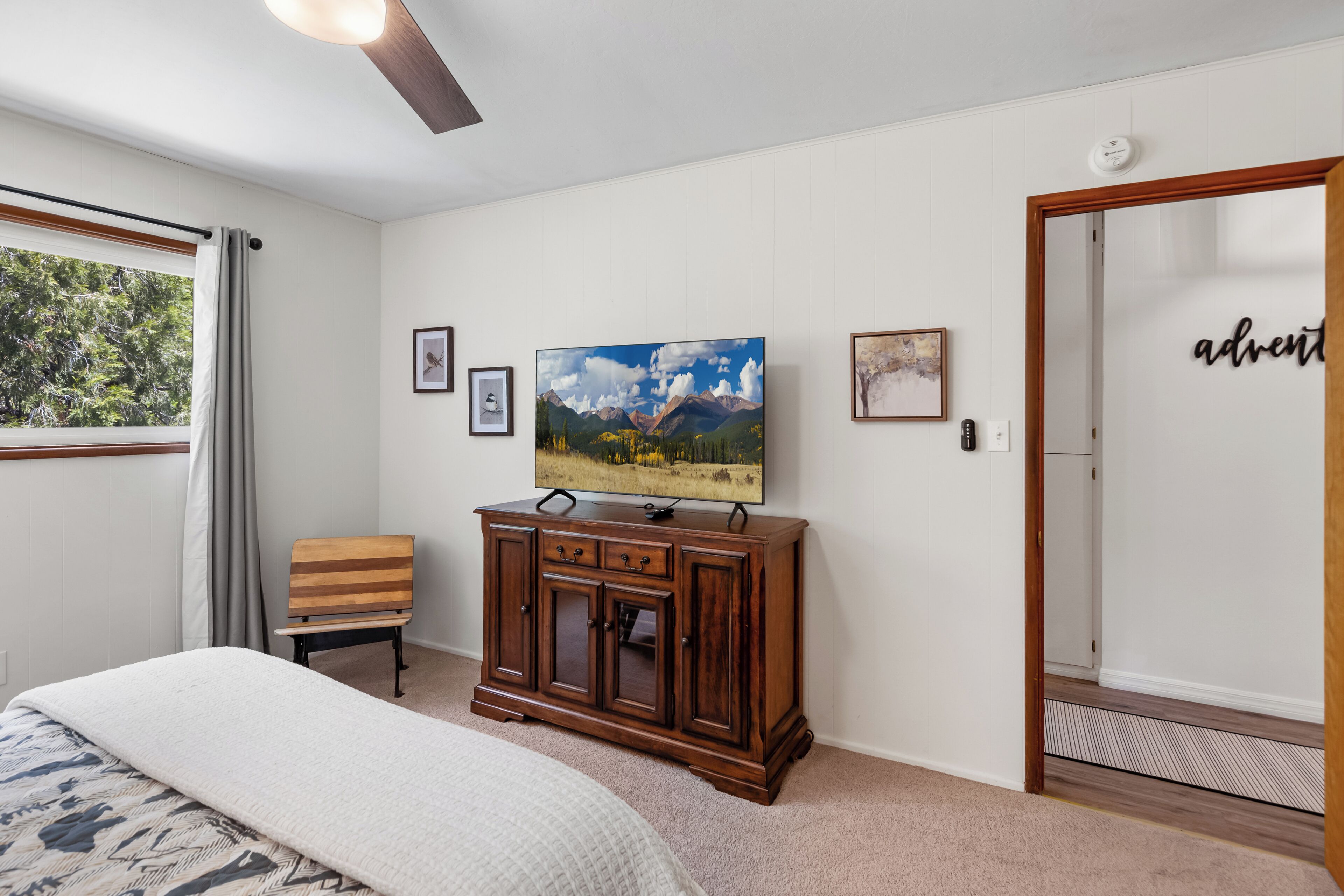 A bedroom with a bed, a wooden cabinet, a television, and a door with a sign.