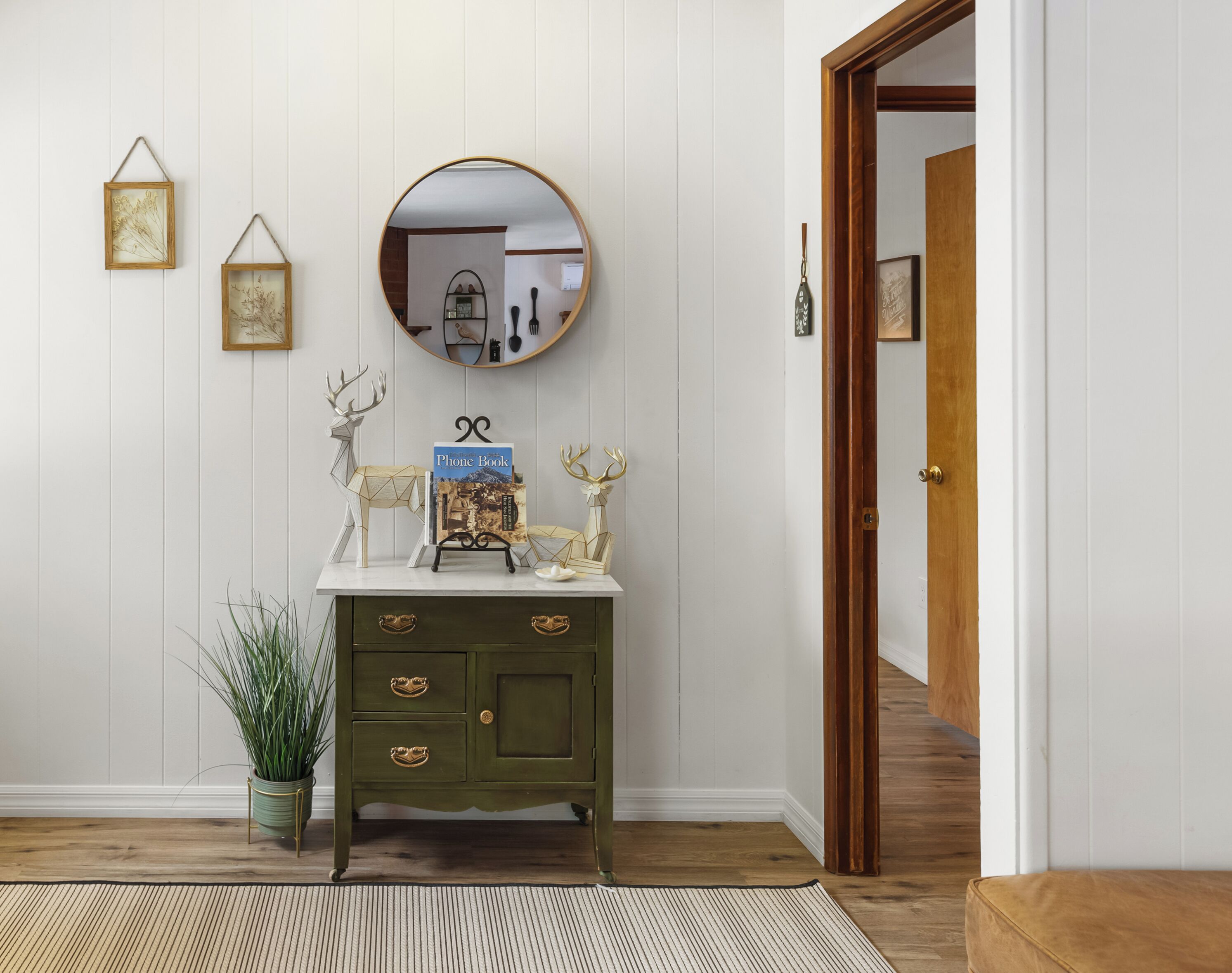 A wooden dresser with a mirror above it, a framed picture, and a plant beside it.