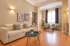 A living room with a beige sofa, a glass coffee table, and a green armchair.