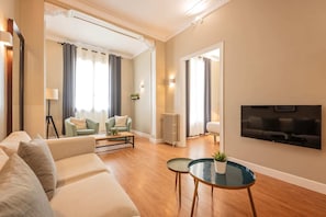 A modern living room with a sofa, two armchairs, a coffee table, a TV, and a radiator. - Sweett | Sepulveda 3C (Barcelona)