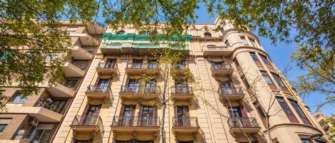 A multi-story building with balconies, a green awning, and a clear blue sky.