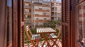 A balcony with a wooden table and chairs, overlooking a residential area with multi-story buildings. - Sweett | Sepulveda 3C (Barcelona)