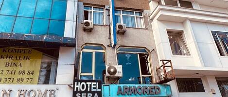 A hotel with a blue entrance, a visible sign for 'Hotel Sera', and a 'BNZ' logo on a car in front.