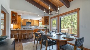 A modern kitchen with wooden cabinets, a central island, and a dining area with a large window. - Carnelian Crest, modern 3BR cabin with hot tub - perfect Couples Retreat! (Carnelian Bay)