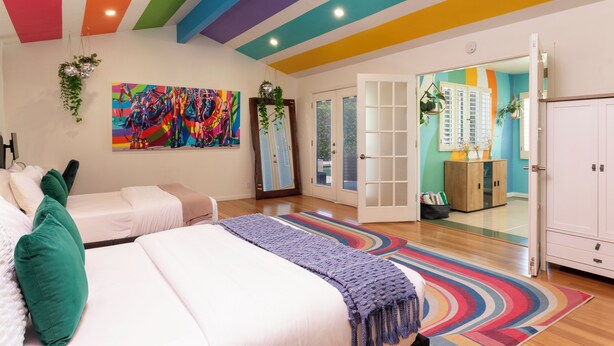 A brightly colored bedroom with two beds, a colorful abstract painting, and a large mirror.