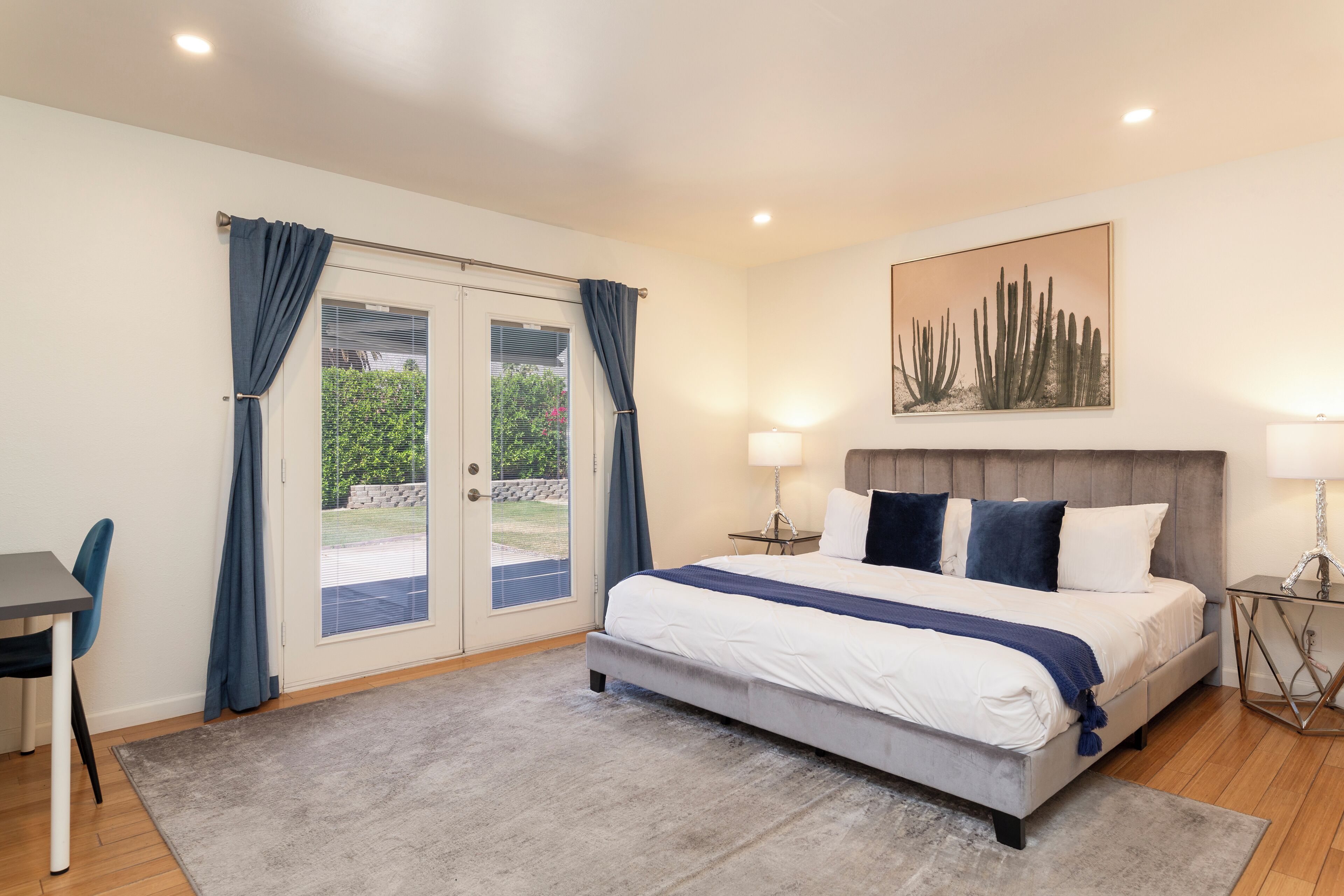 A bedroom with a bed, two bedside lamps, a nightstand, a chair, a door with curtains, and a painting on the wall.