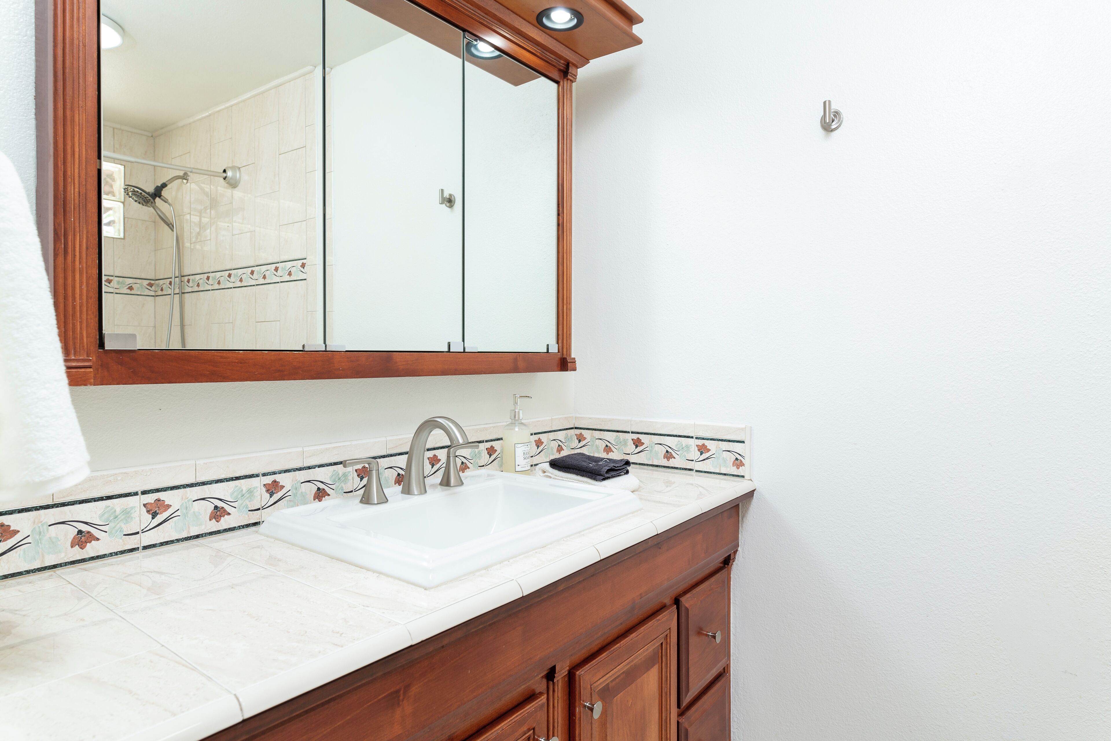 Un baño con lavamanos blanco, tocador de madera y un espejo grande.