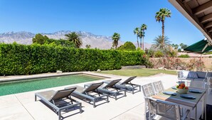A poolside area with lounge chairs, a table with fruit, and a view of mountains.