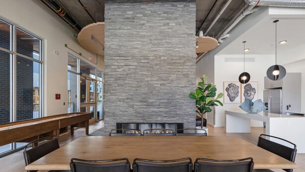 Un espace de salle à manger moderne avec une longue table en bois, des chaises noires et un mur d’accent en pierre.