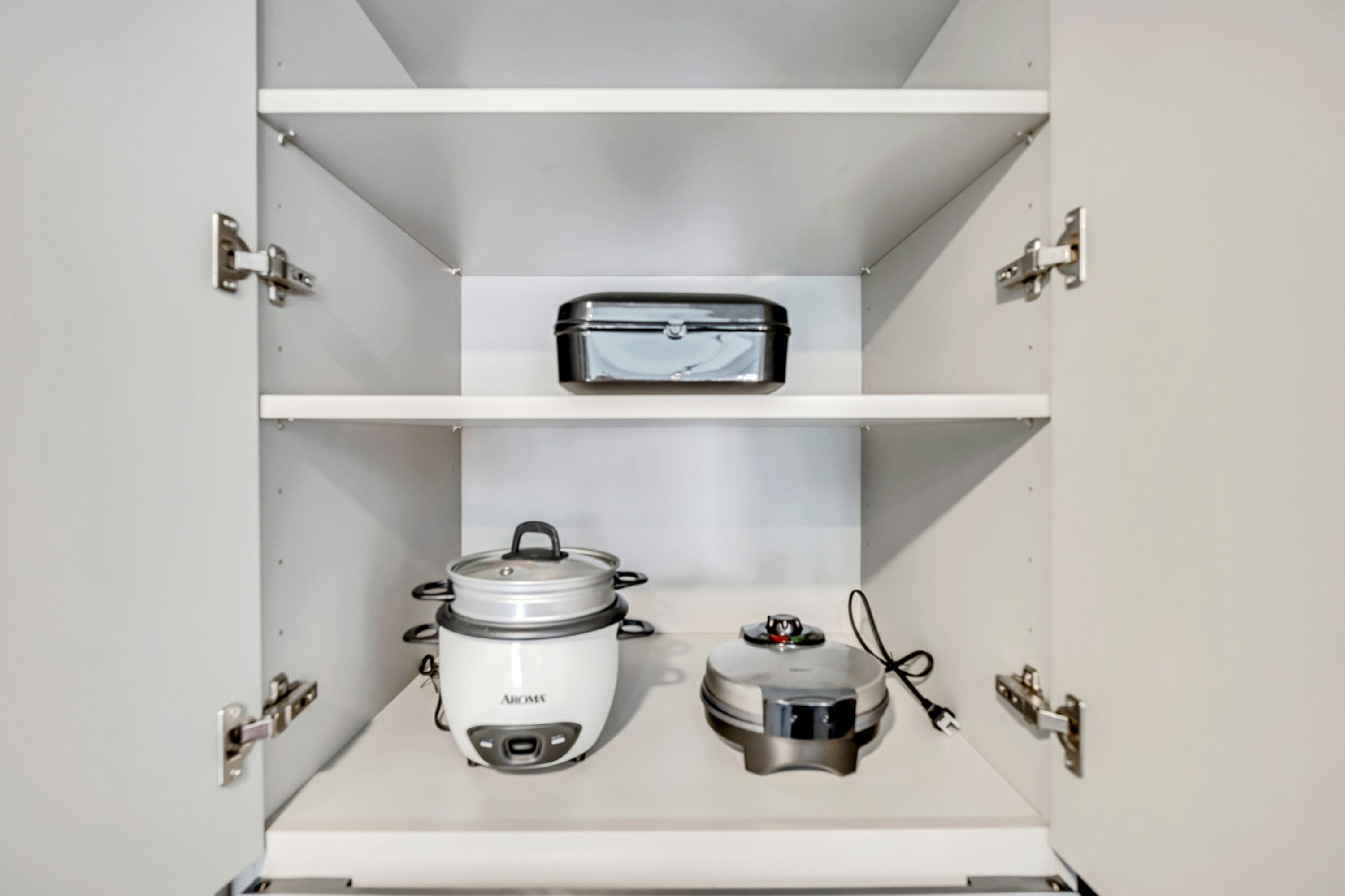 A kitchen with white cabinets and a countertop. There is a rice cooker and a small appliance on the counter.