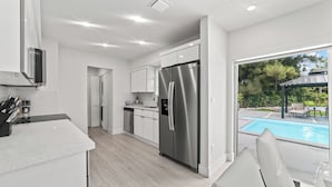 A modern kitchen with white cabinets, a stainless steel refrigerator, and a view of a swimming pool. - New Home w/ Big Patio / Heated Pool / Pool table / Ping pong table (Miami Gardens)
