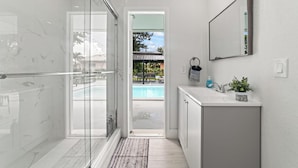 A modern bathroom with a glass shower enclosure, a sink with a mirror, and a view of a pool outside. - New Home w/ Big Patio / Heated Pool / Pool table / Ping pong table (Miami Gardens)