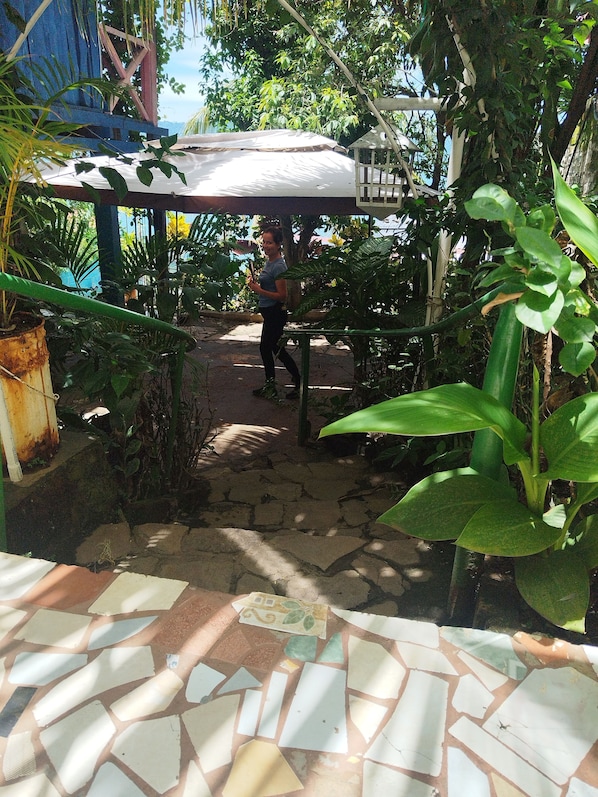 A pathway leading to a covered area with a tiled floor and lush greenery. - Hostal y Restaurante Tiki Island (Santa Ana)