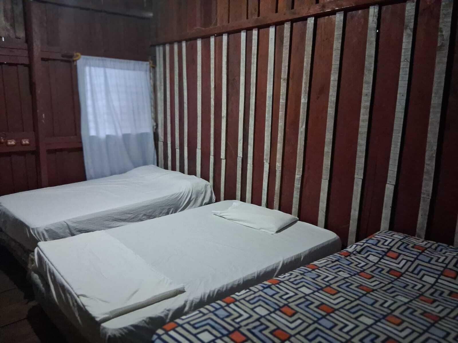 A room with two single beds, a wooden headboard, and a curtain.