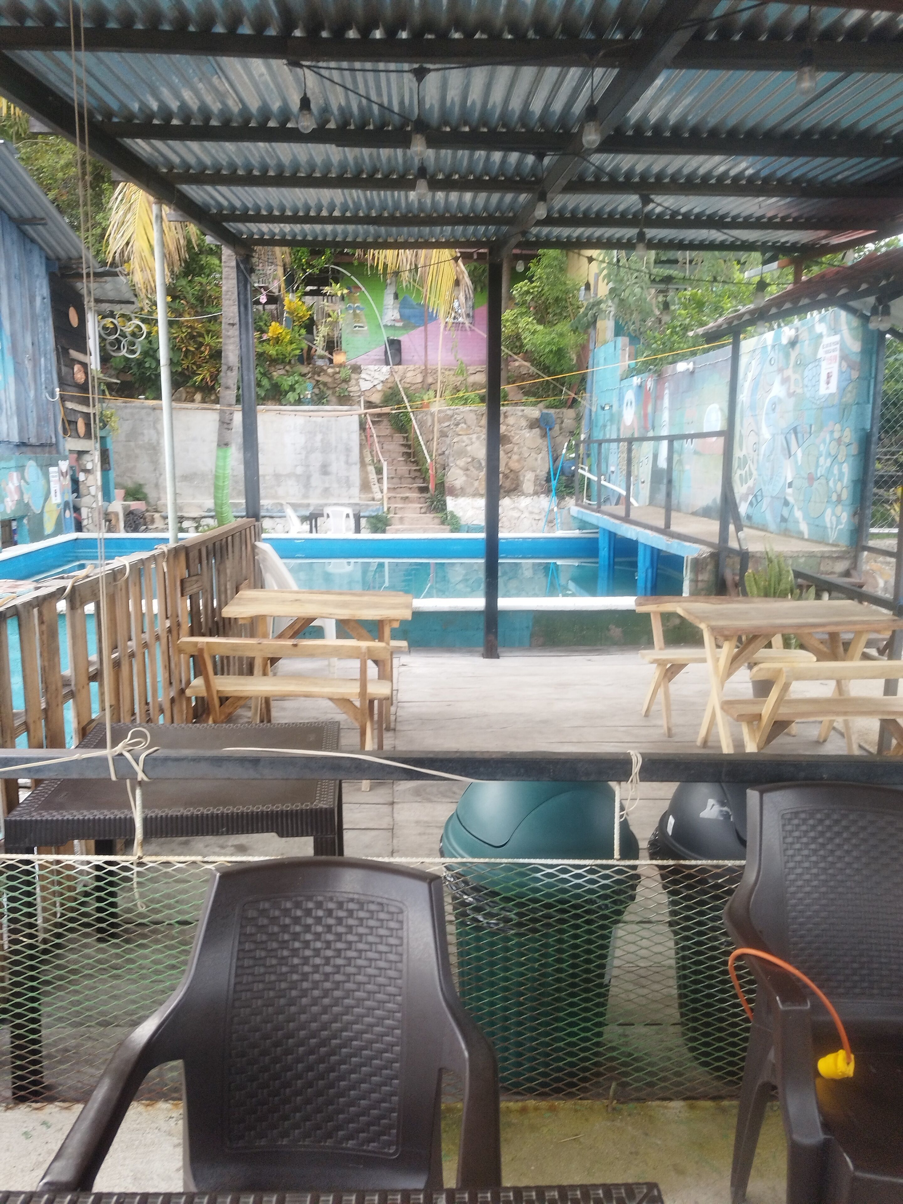 Un espacio al aire libre techado con piscina, mesas y sillas de madera.