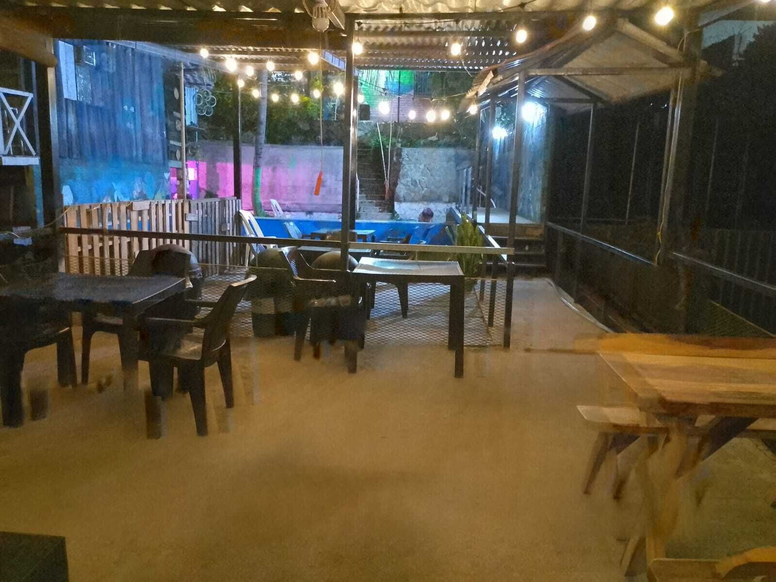 An outdoor patio area with tables and chairs, a pool, and string lights.
