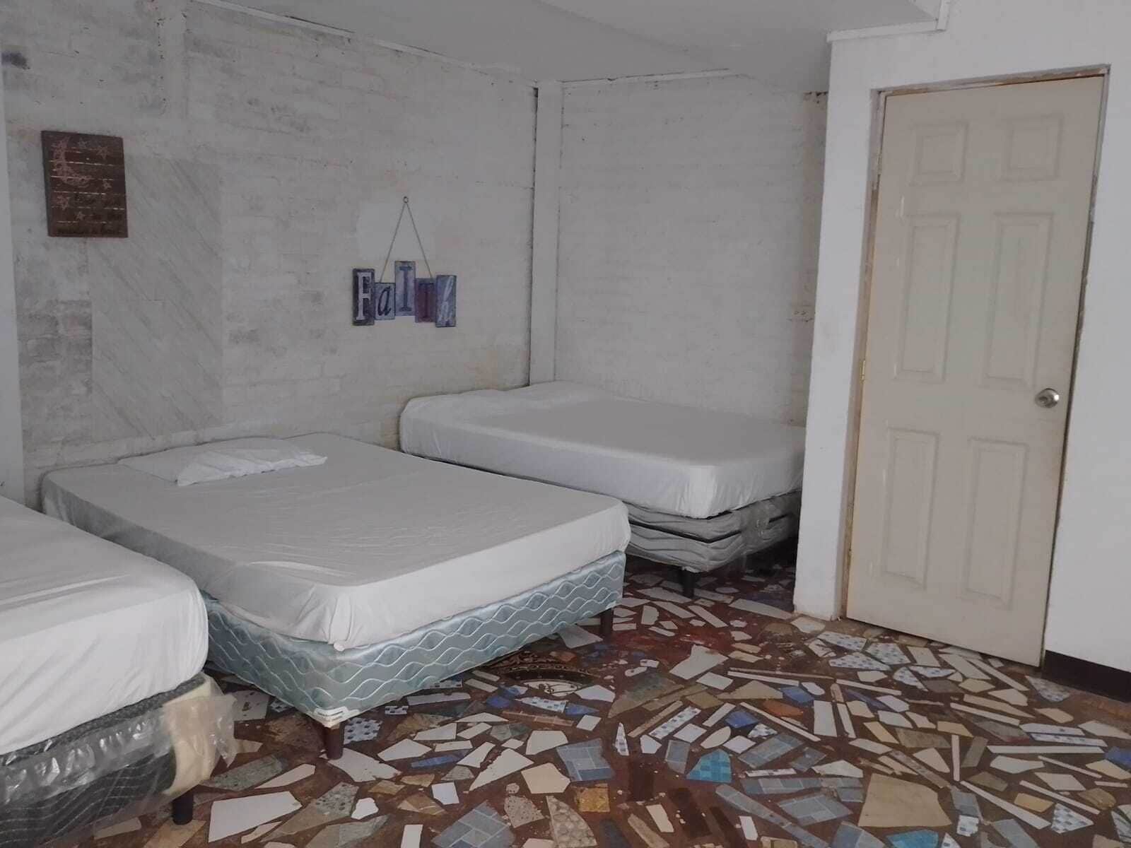 A room with three beds, a tiled floor, and a white door.
