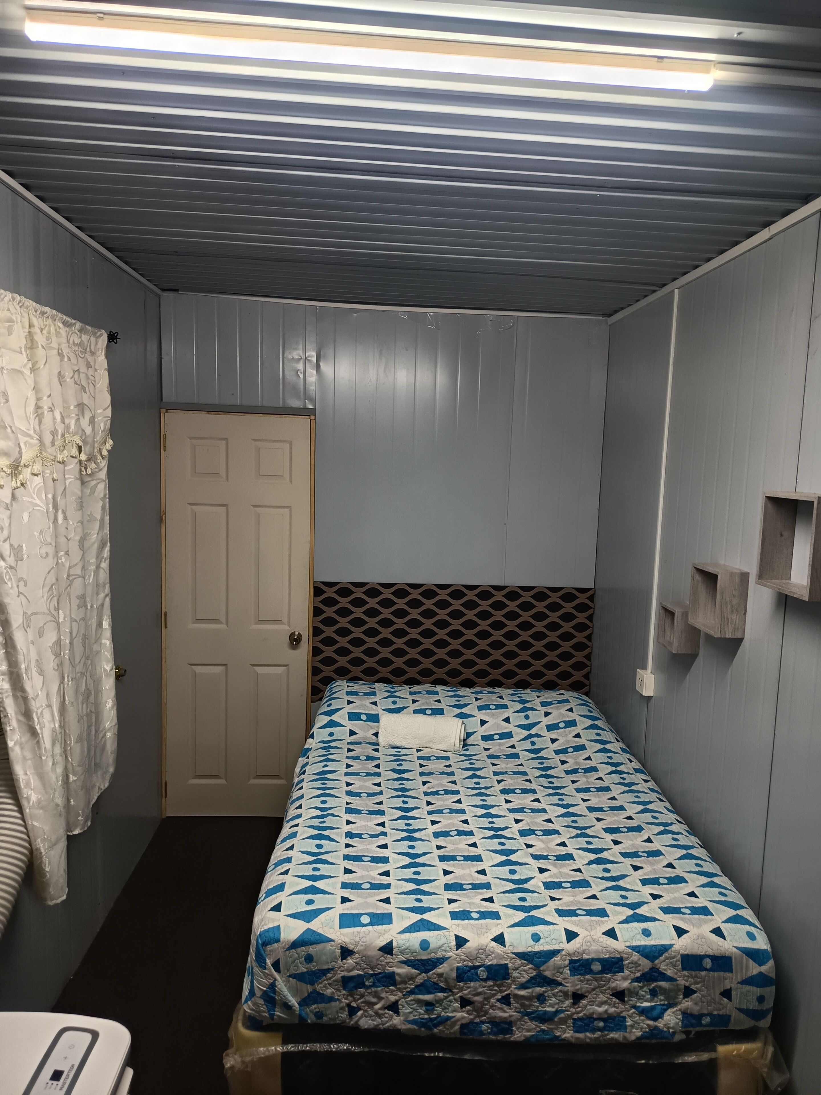 A room with a bed, a door, and a wall-mounted shelf.