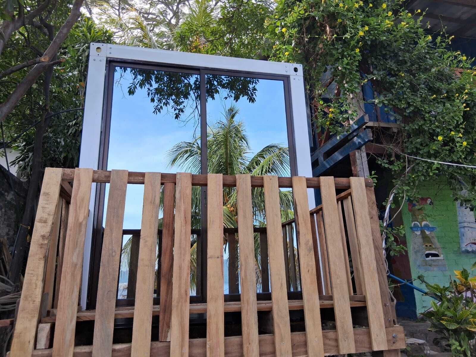 Ein Zimmer mit großem Fenster, Holzlamellen und Blick auf Palmen.