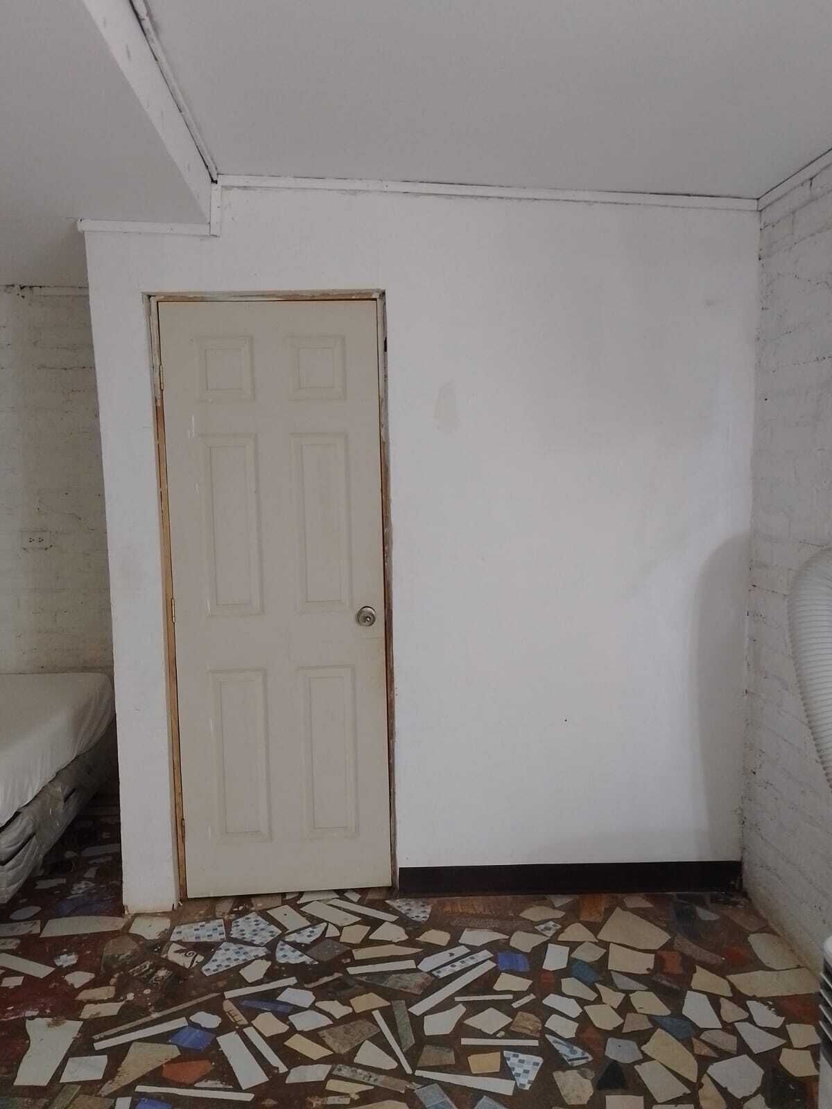 Habitació amb una porta blanca, un matalàs a l'esquerra i un sòl amb un disseny mosaic.