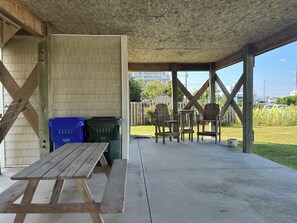An outdoor covered patio with a wooden table and chairs, a trash bin, and a view of a residential area.