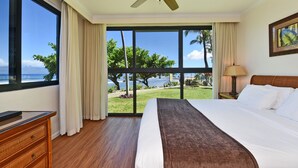 A hotel room with a large bed, a ceiling fan, a view of the ocean, and a wooden dresser.