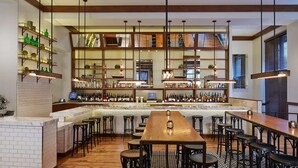 A bar area with a long wooden table, multiple stools, and shelves stocked with bottles. - Near Downtown Atlanta | Pet-friendly. Gym. Dining (Atlanta)