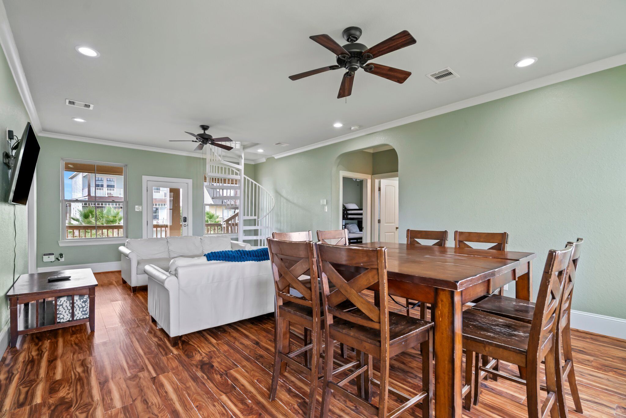 A spacious living room with a wooden dining table, white sofa, and ceiling fans.